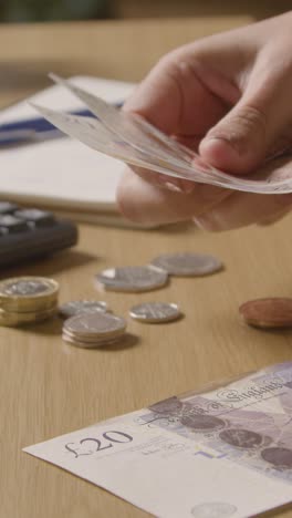 Vertical-Video-Of-Woman-With-Sterling-Notes-And-Coins-Using-Calculator-To-Budget-For-Household-Bills-In-Cost-Of-Living-Crisis